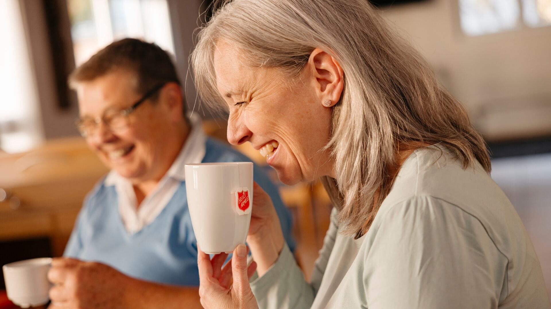 Zwei Personen trinken gemeinsam Kaffee und Tee und lachen bei der Heilsarmee Affoltern am Albis.